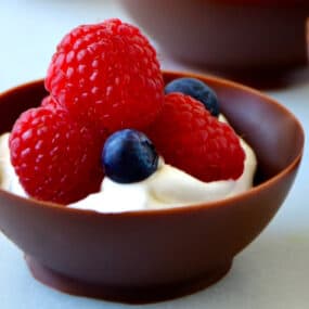 Closeup view of chocolate balloon bowl containing whipped cream topped with raspberries and blueberries