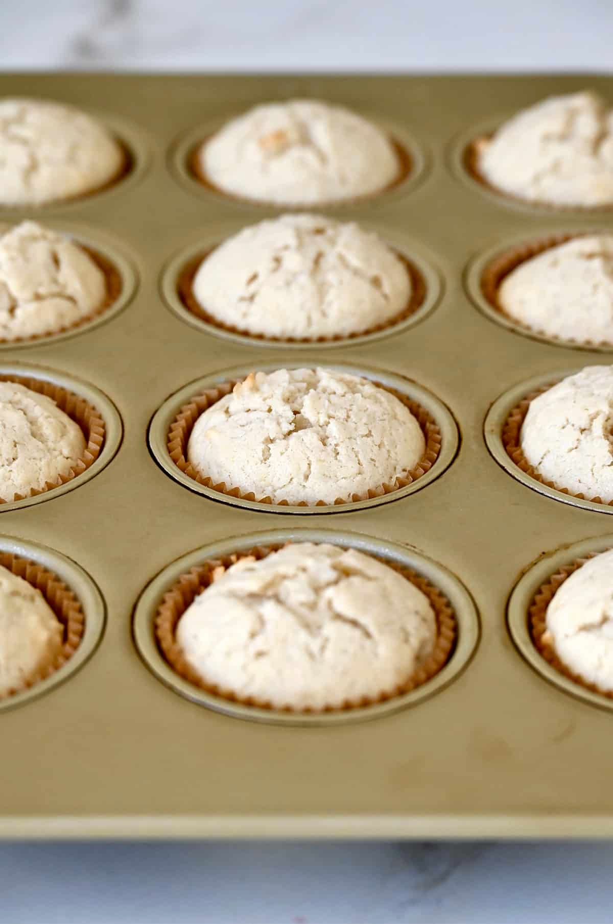 Baked coconut cupcakes in a lined muffin pan.