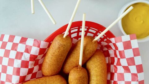 Red food basket filled with Easy Homemade Mini Corn Dogs next to small ramekins with ketchup and mustard