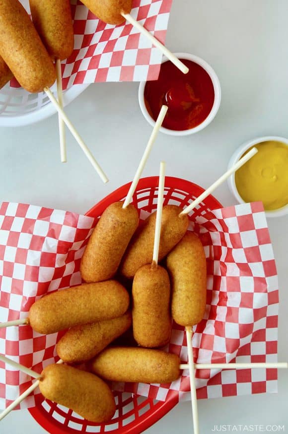 Red food basket filled with Easy Homemade Mini Corn Dogs next to small ramekins with ketchup and mustard 