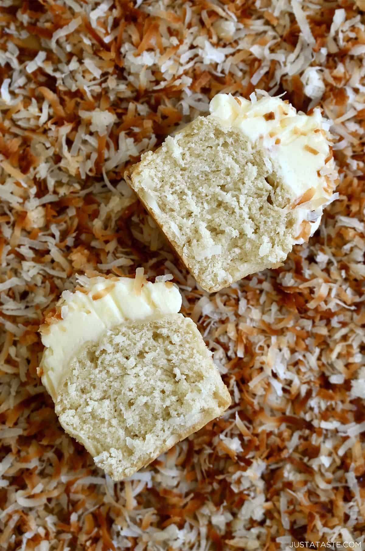 A coconut cupcake cut in half on a bed of toasted coconut flakes.