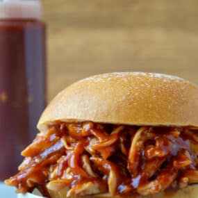 Pulled pork doused in Easy Homemade Root Beer Barbecue Sauce sandwiched between two hamburger bun halves.