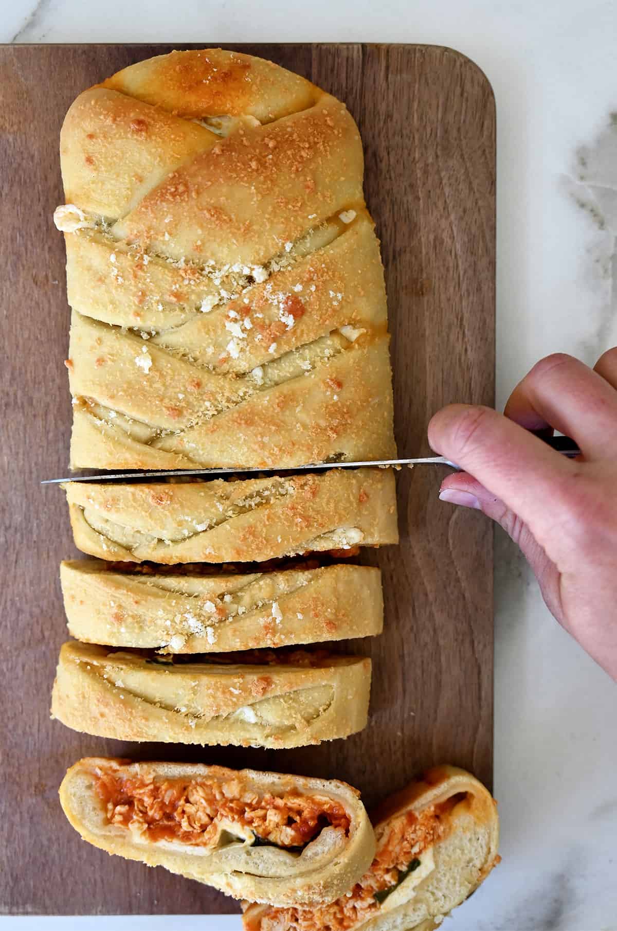 A hand holding a sharp knife cuts a chicken Stromboli into slices to serve.