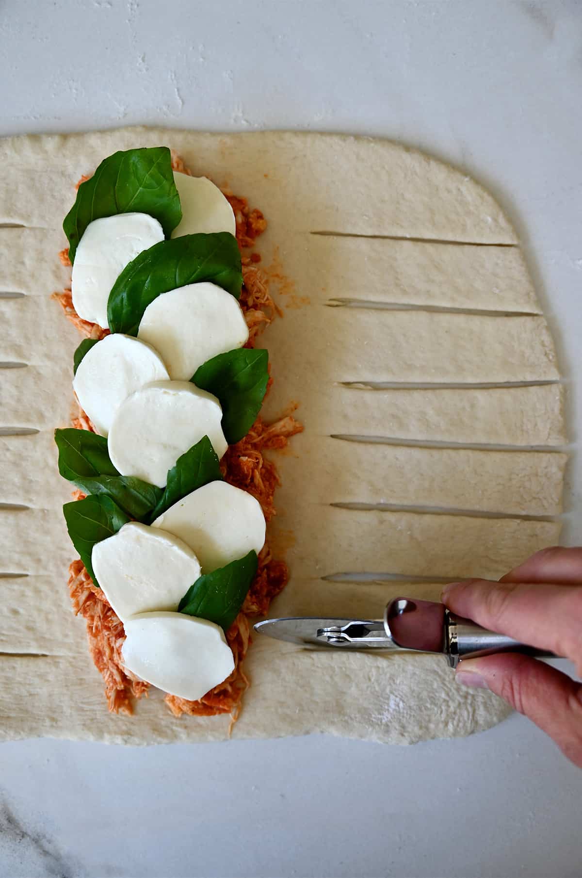A hand holding a pizza wheel cuts slits into dough topped with Stromboli fillings.
