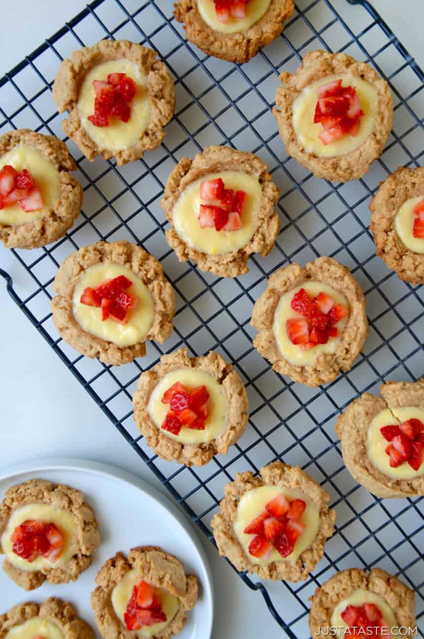  Top-down view of cheesecake cookies topped with chopped fresh strawberries on a wire cooling rack. 