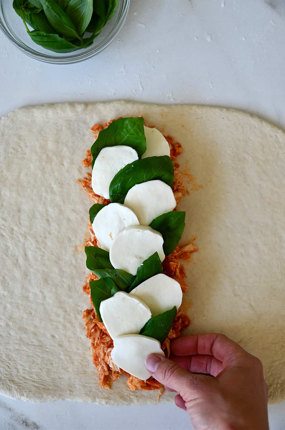 Pizza dough topped with shredded chicken, mozzarella slices and basil leaves.