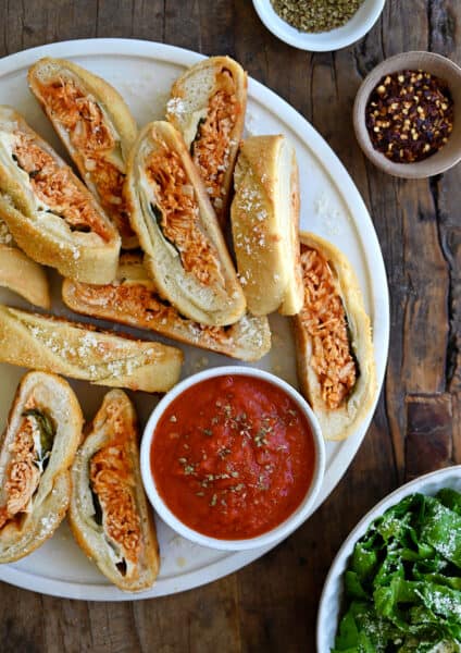 Slices of Stromboli on a round serving platter along with a small bowl containing marinara sauce.