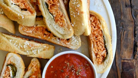 Slices of Stromboli on a round serving platter along with a small bowl containing marinara sauce.