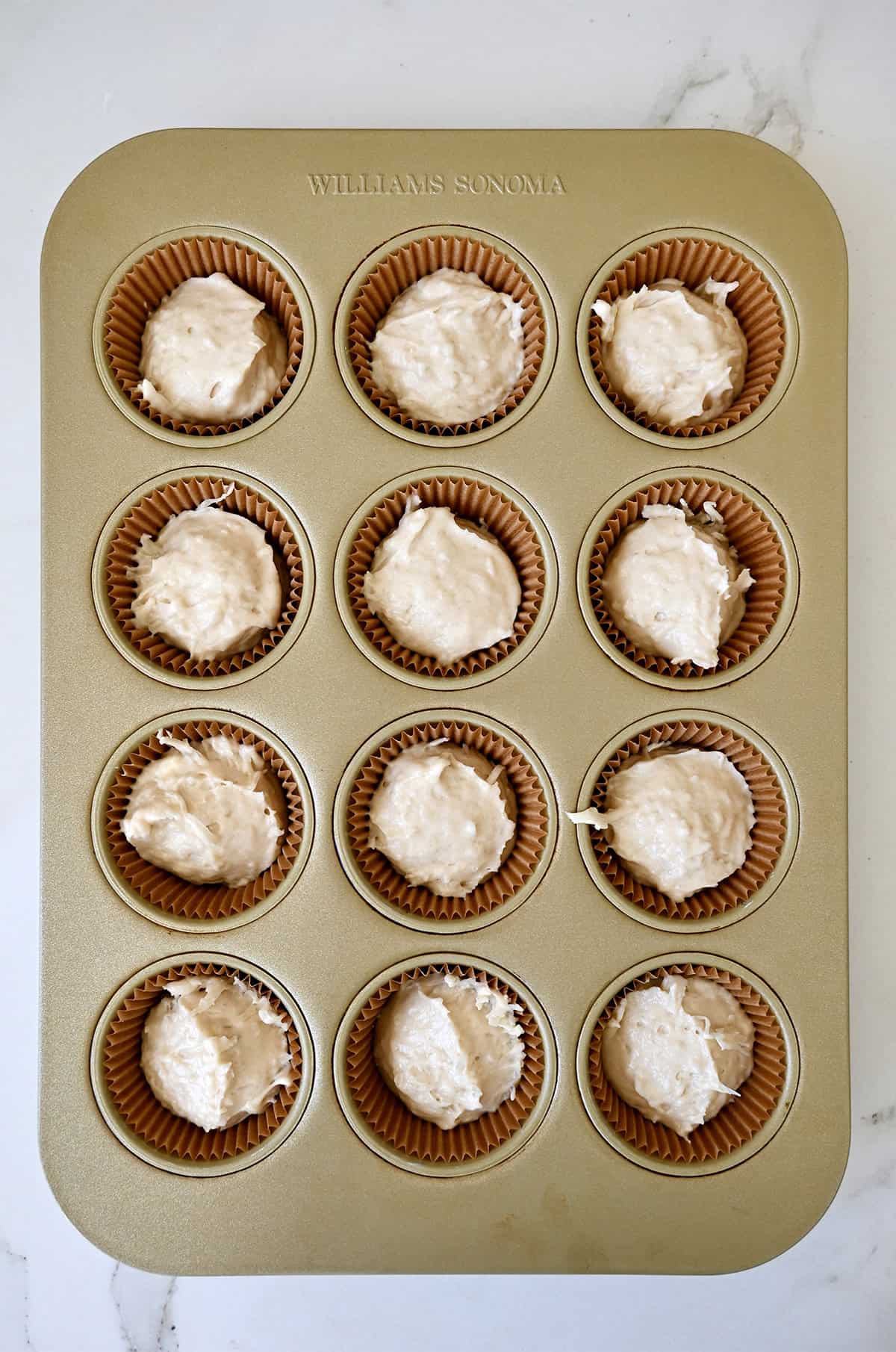 Coconut cupcake batter divided amongst a 12-cup lined muffin tin.