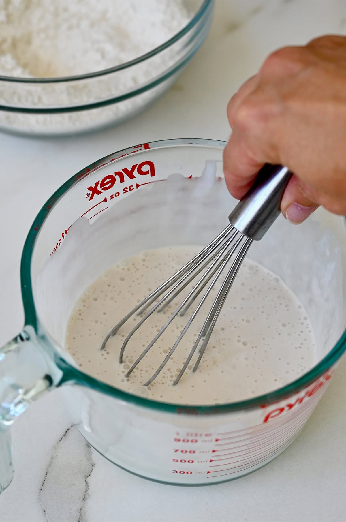 Whisking wet ingredients for coconut milk cupcakes in a large liquid measuring cup.