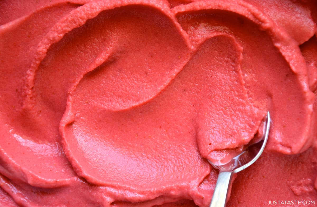 A close-up view of a spoon swirled into creamy strawberry frozen yogurt.