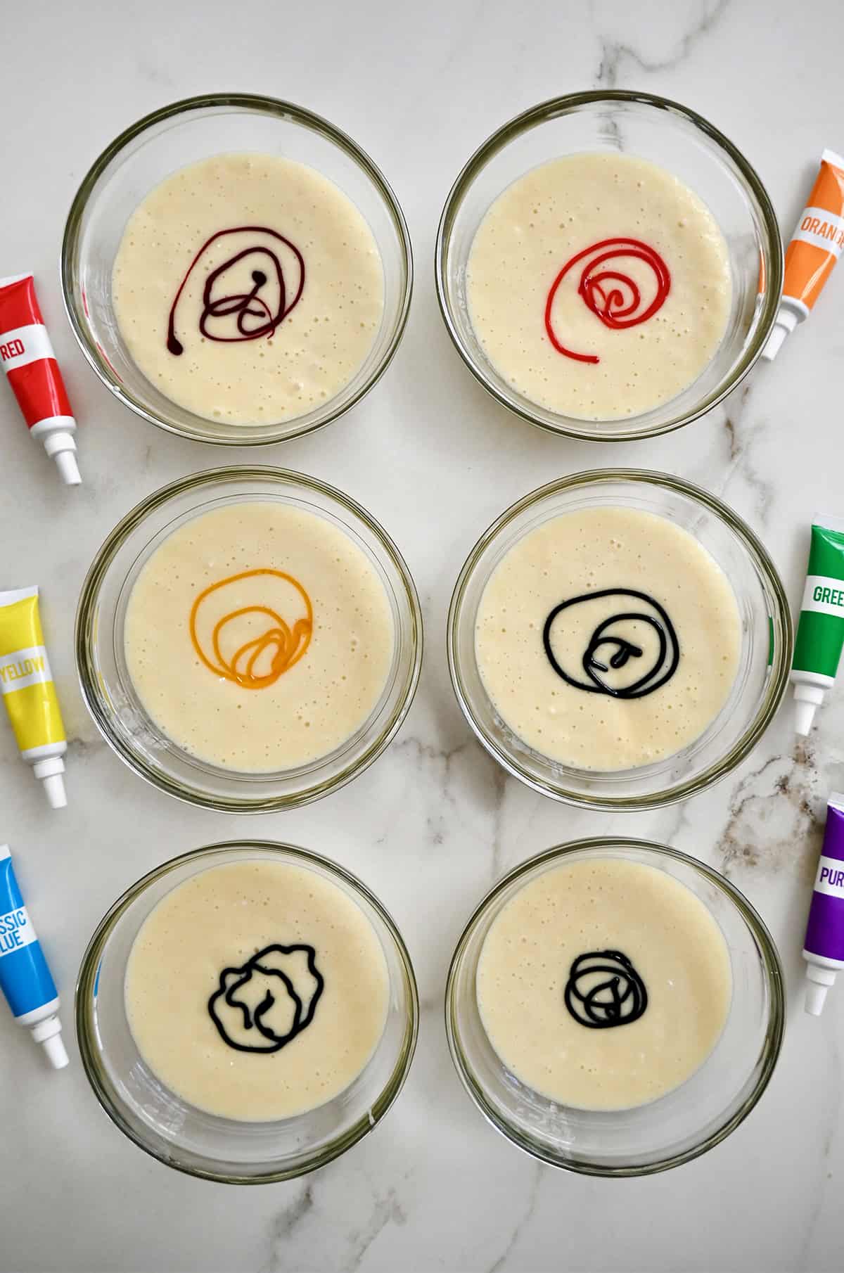 Adding food coloring to small bowls containing cake batter.