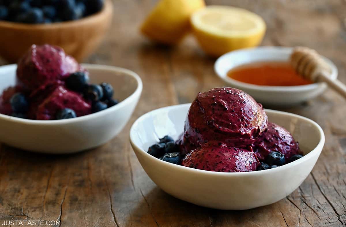 Three scoops of blueberry frozen yogurt in a white bowl with fresh blueberries.