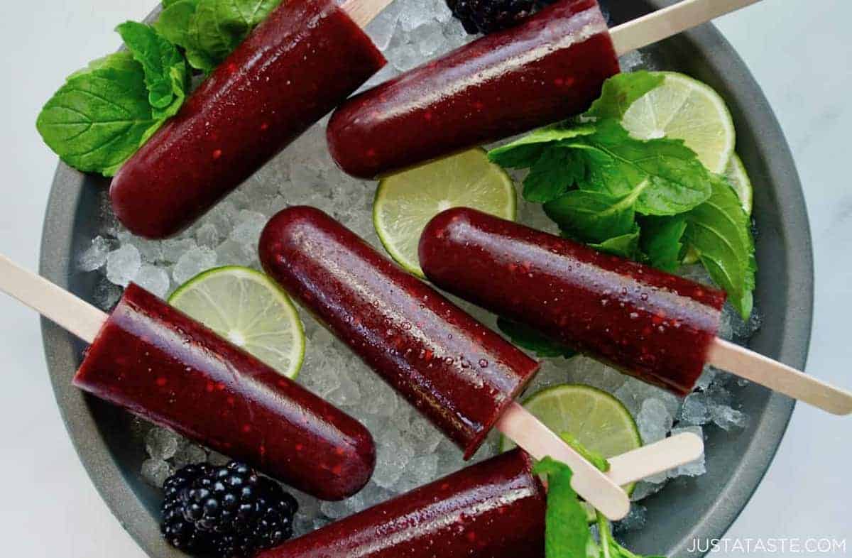 A top-down view of blackberry mojito popsicles over ice with lime wedges and fresh mint leaves.