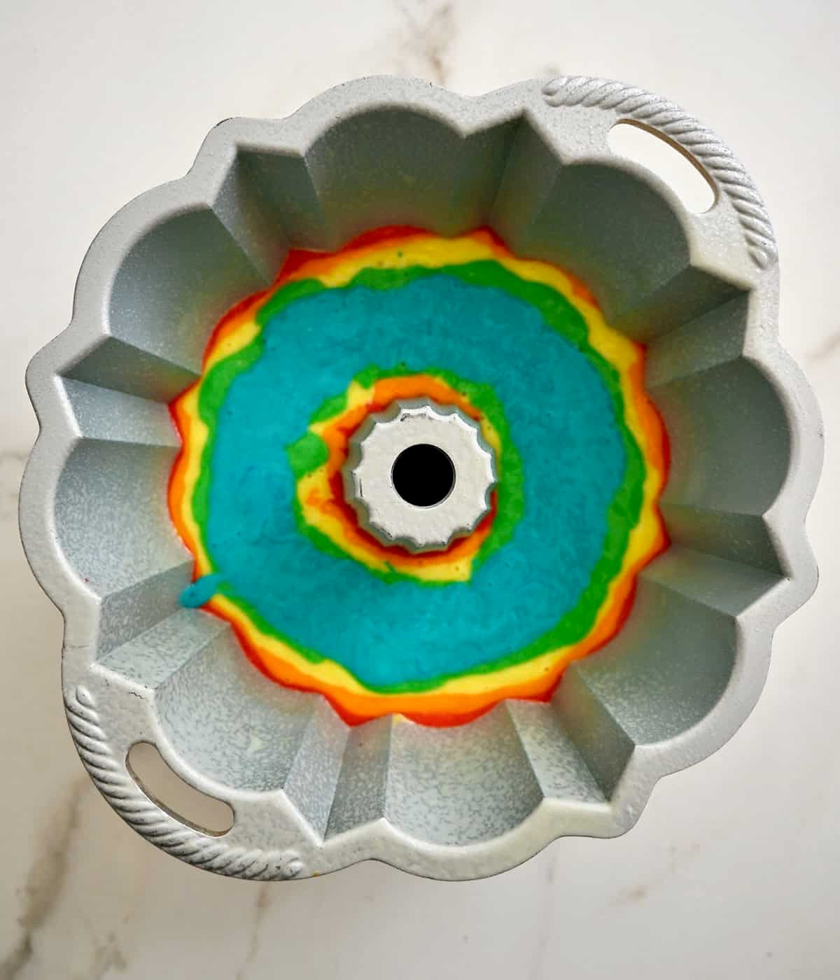 Blue cake layer atop green, yellow, orange and red cake layers in a bundt pan.