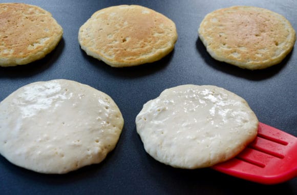 Red spatula flipping flapjacks on griddle
