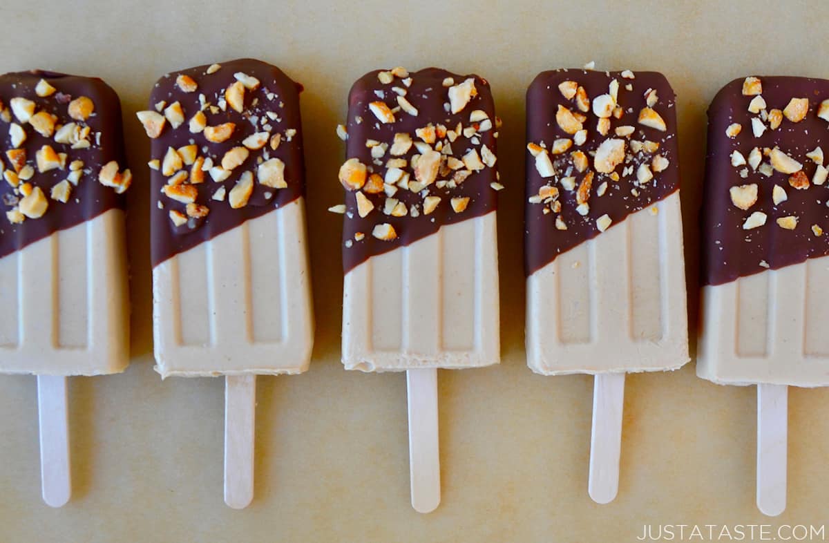 A row of peanut butter frozen yogurt pops that have been dipped in chocolate and sprinkled with chopped peanuts.