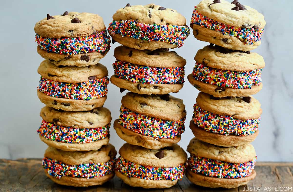 Three tall stacks of chocolate chip cookie ice cream sandwiches that have been rolled in rainbow sprinkles.