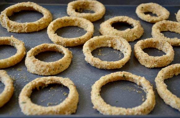 A baking sheet with unbaked onion rings on top