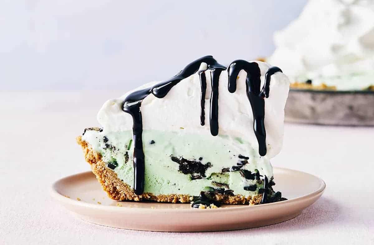 A slice of mint ice cream pie topped with whipped cream and drizzled with melted chocolate. 