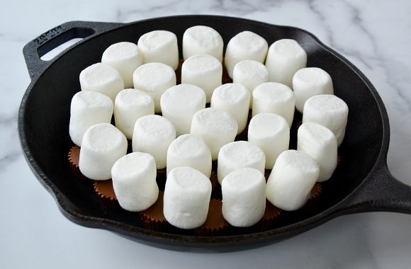 Marshmallows stacked atop peanut butter cups in a cast-iron skillet