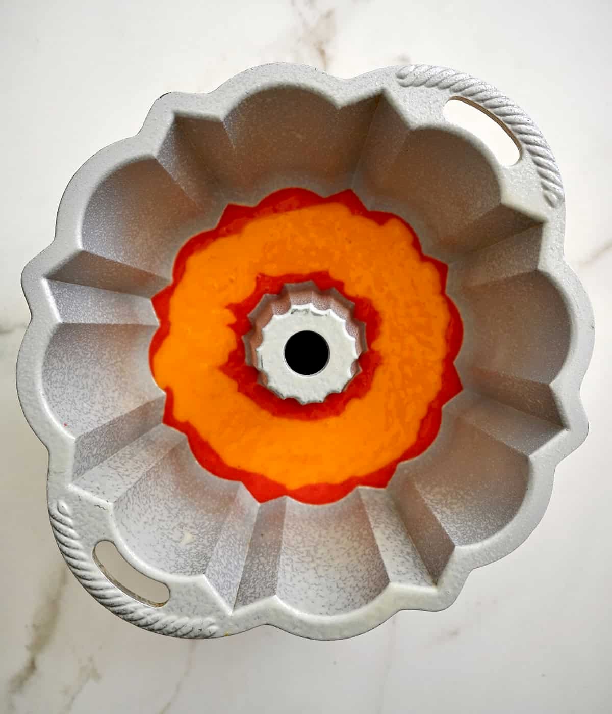 Orange layer of a rainbow bundt cake atop red cake batter.