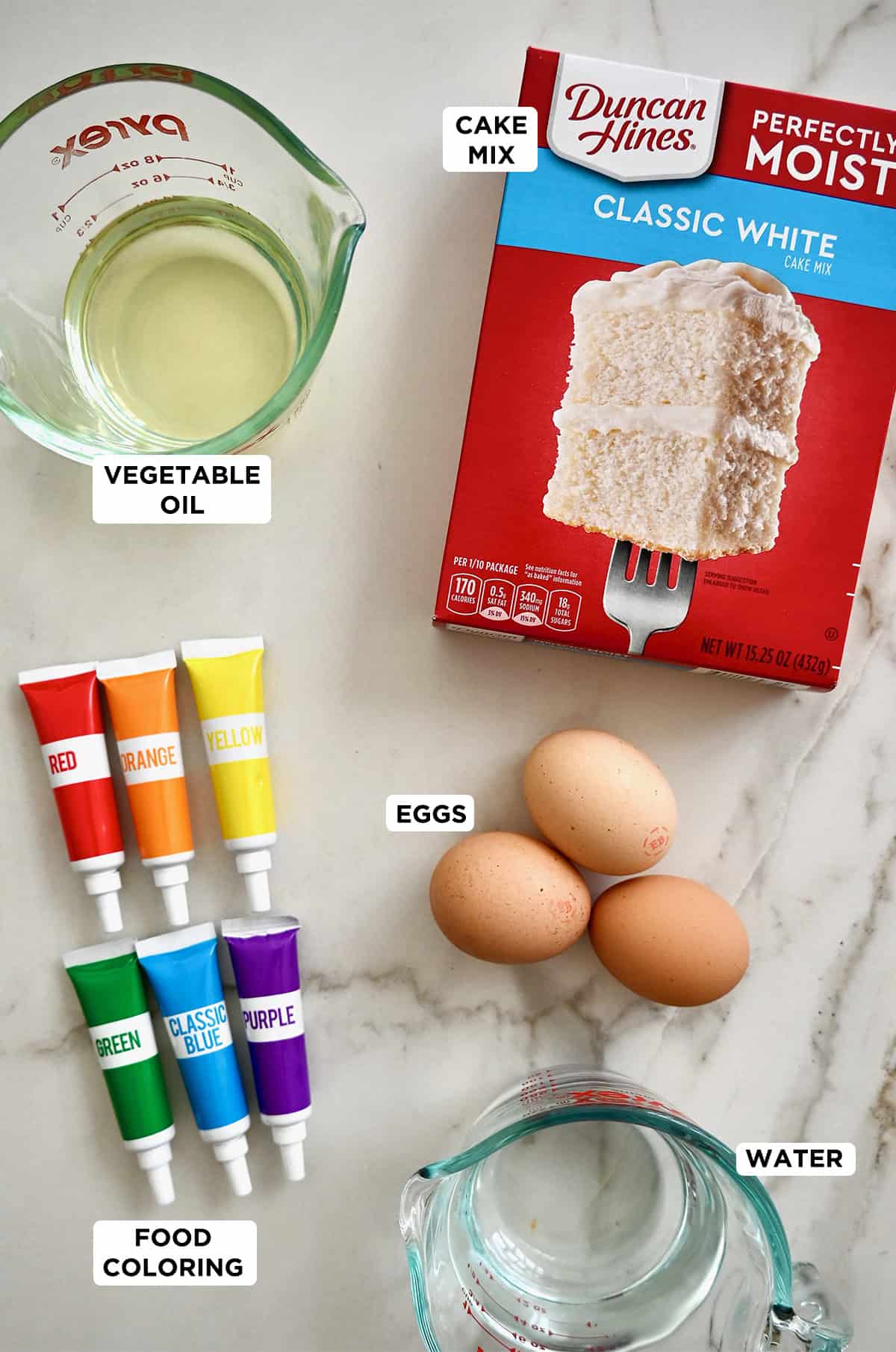 Rainbow cake ingredients: A box of white cake mix, vegetable oil, eggs, food coloring and water.