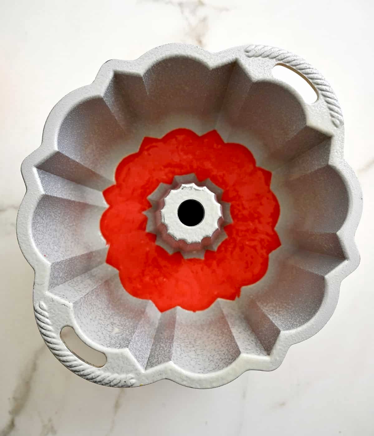 A bundt pan containing red cake batter.