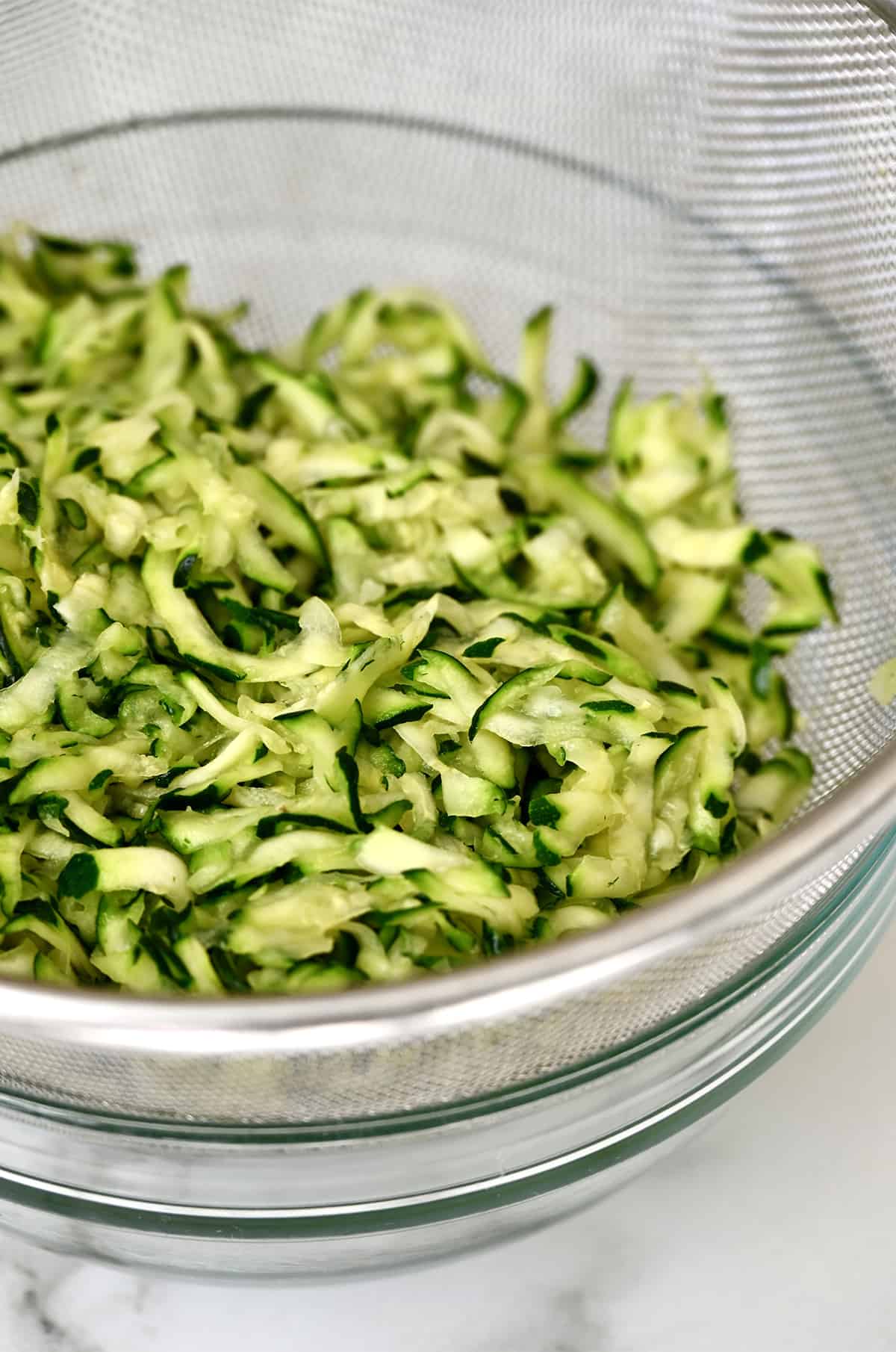 Zucchini in a mesh sieve over a glass bowl.