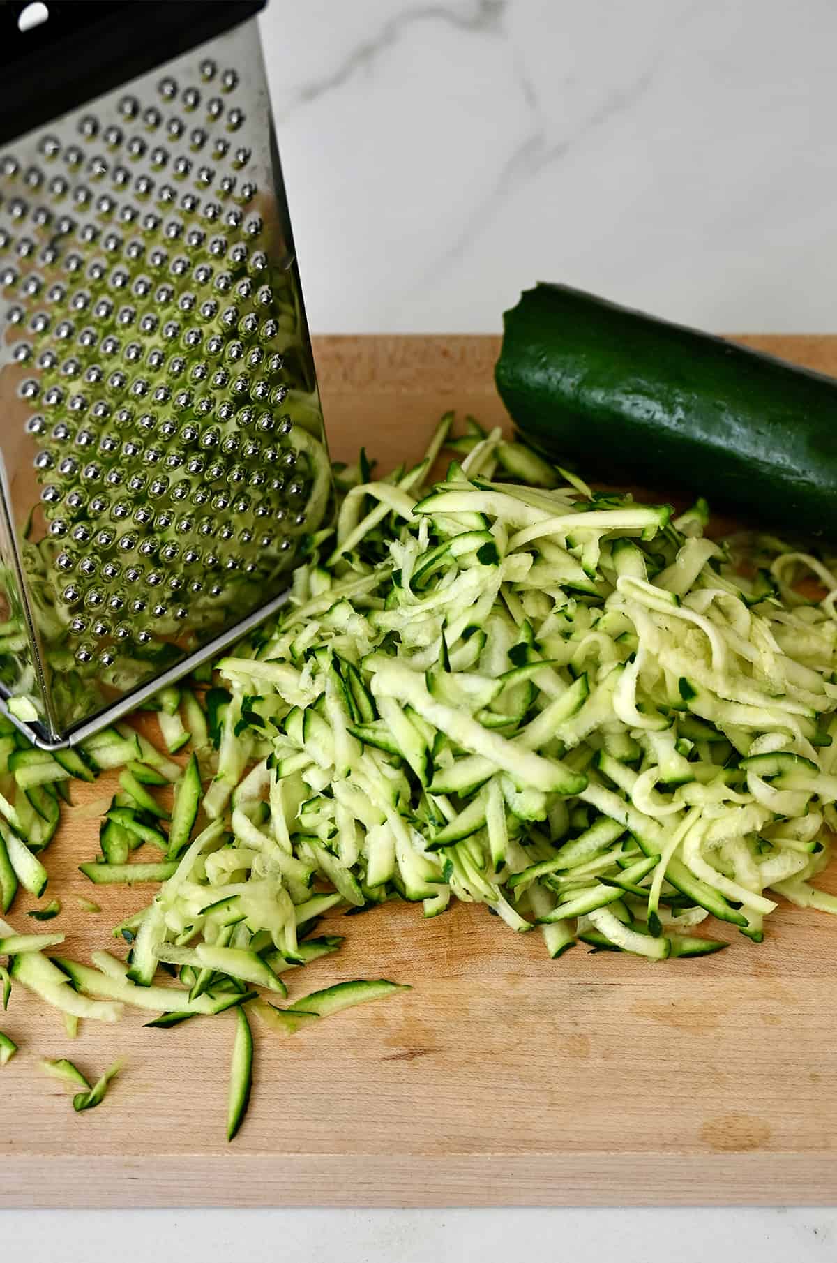 Shredded zucchini next to a box grater.