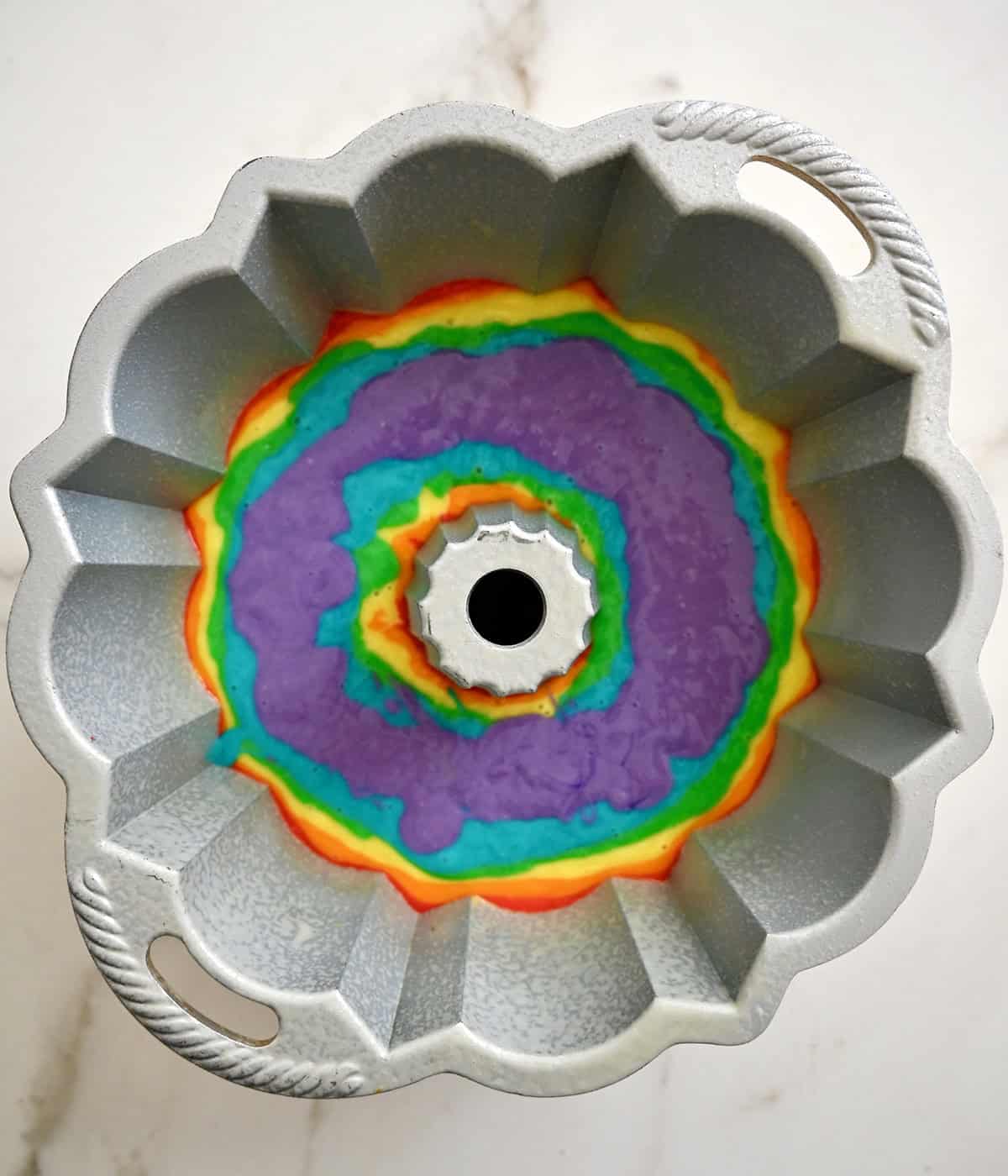 A bundt pan containing all six layers of a rainbow cake: red, orange, yellow, green, blue and purple.