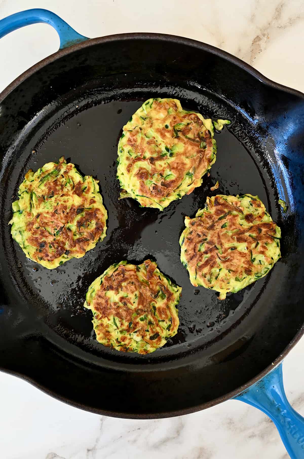 Four crispy zucchini fritters in a large skillet.