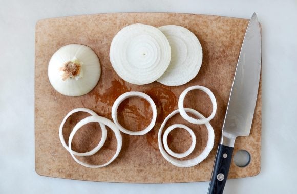 A wood cutting board with sliced onions and a knife