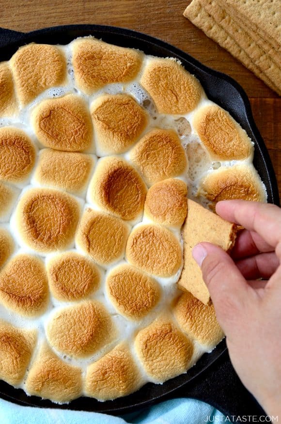 A hand dunking a graham cracker into s'mores dip