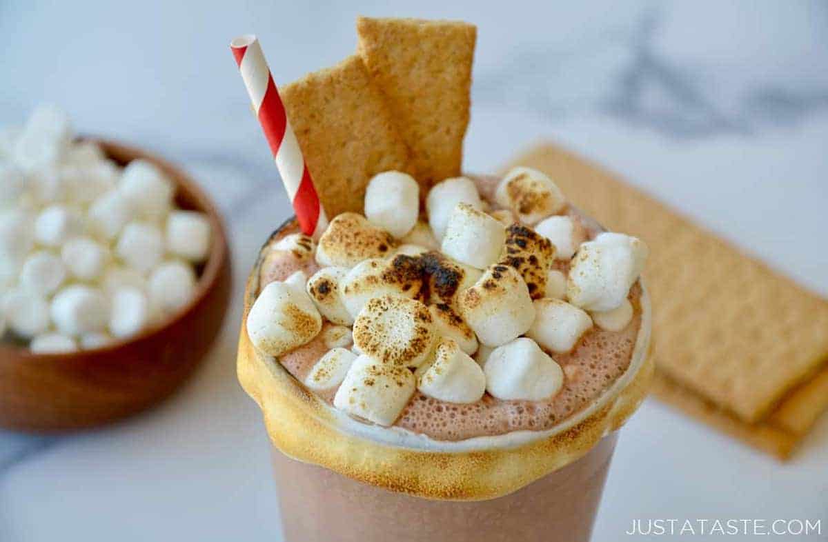 A closeup view of a s'mores milkshake topped with roasted mini marshmallows and a graham cracker.