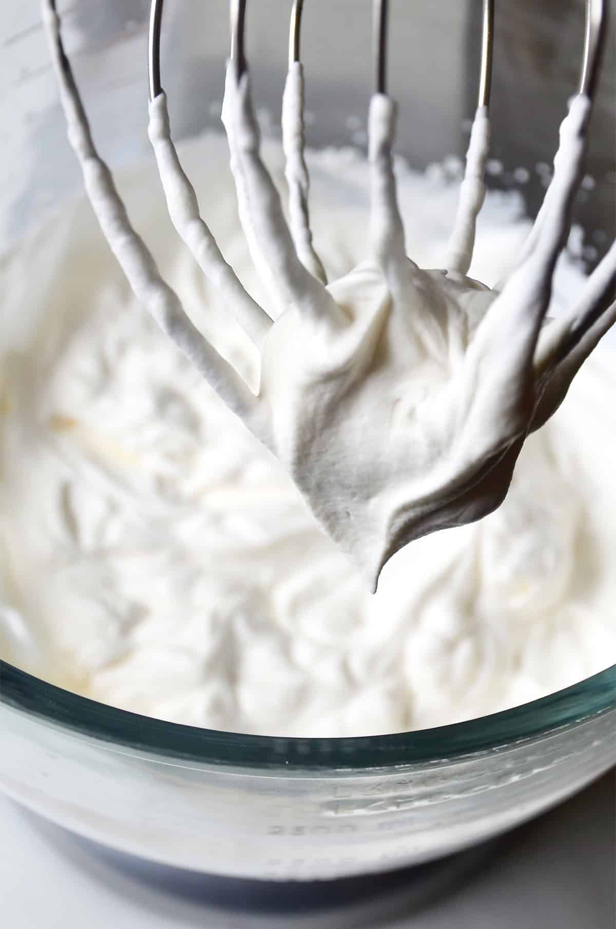 Stiff peaks of homemade tangy whipped cream on the whisk attachment of a stand mixer.