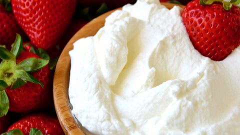 Homemade whipped cream in a bowl on a plate surrounded by strawberries.