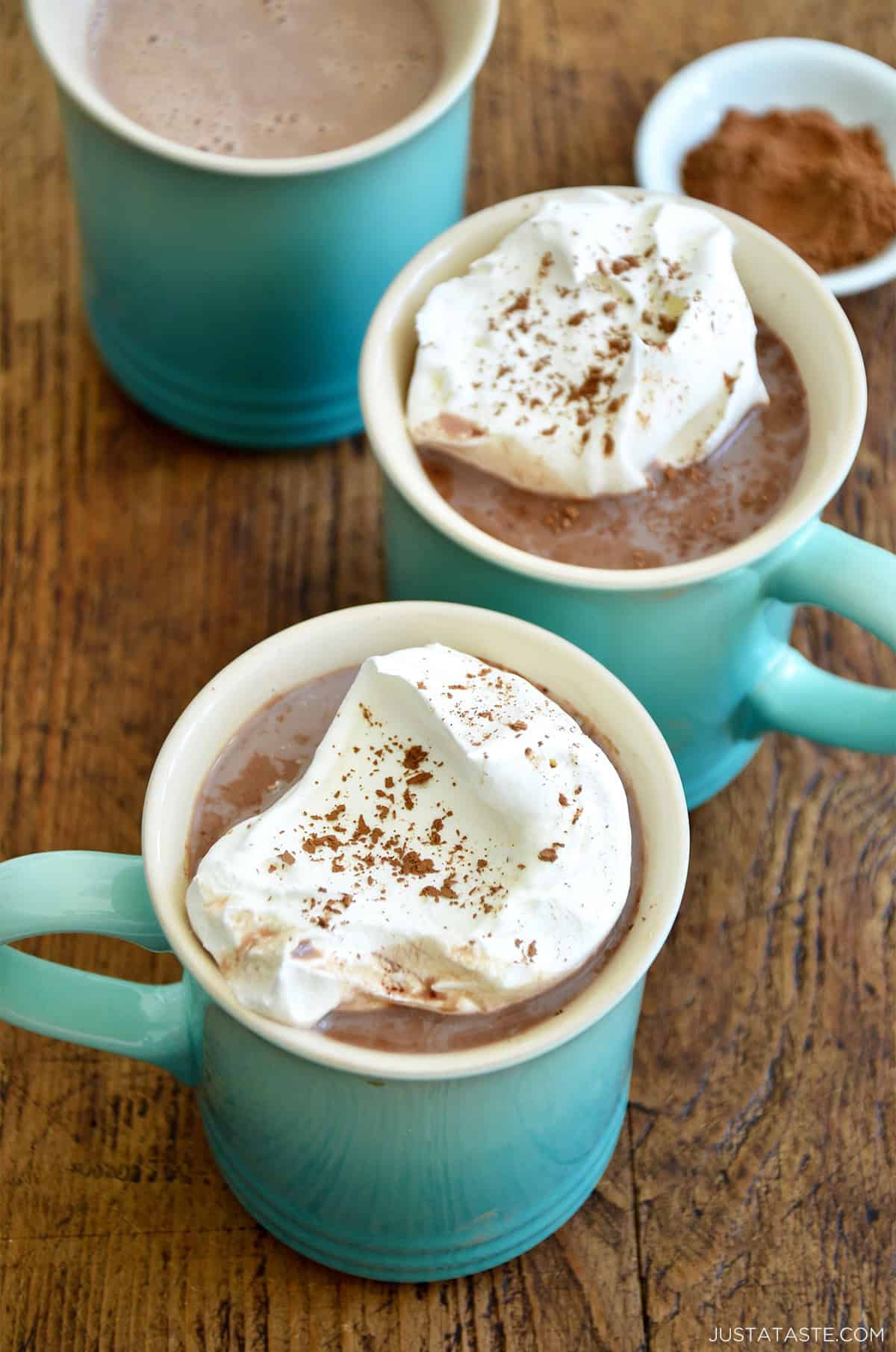 Two mugs with hot cocoa topped with a dollop of sweet and tangy homemade whipped cream.