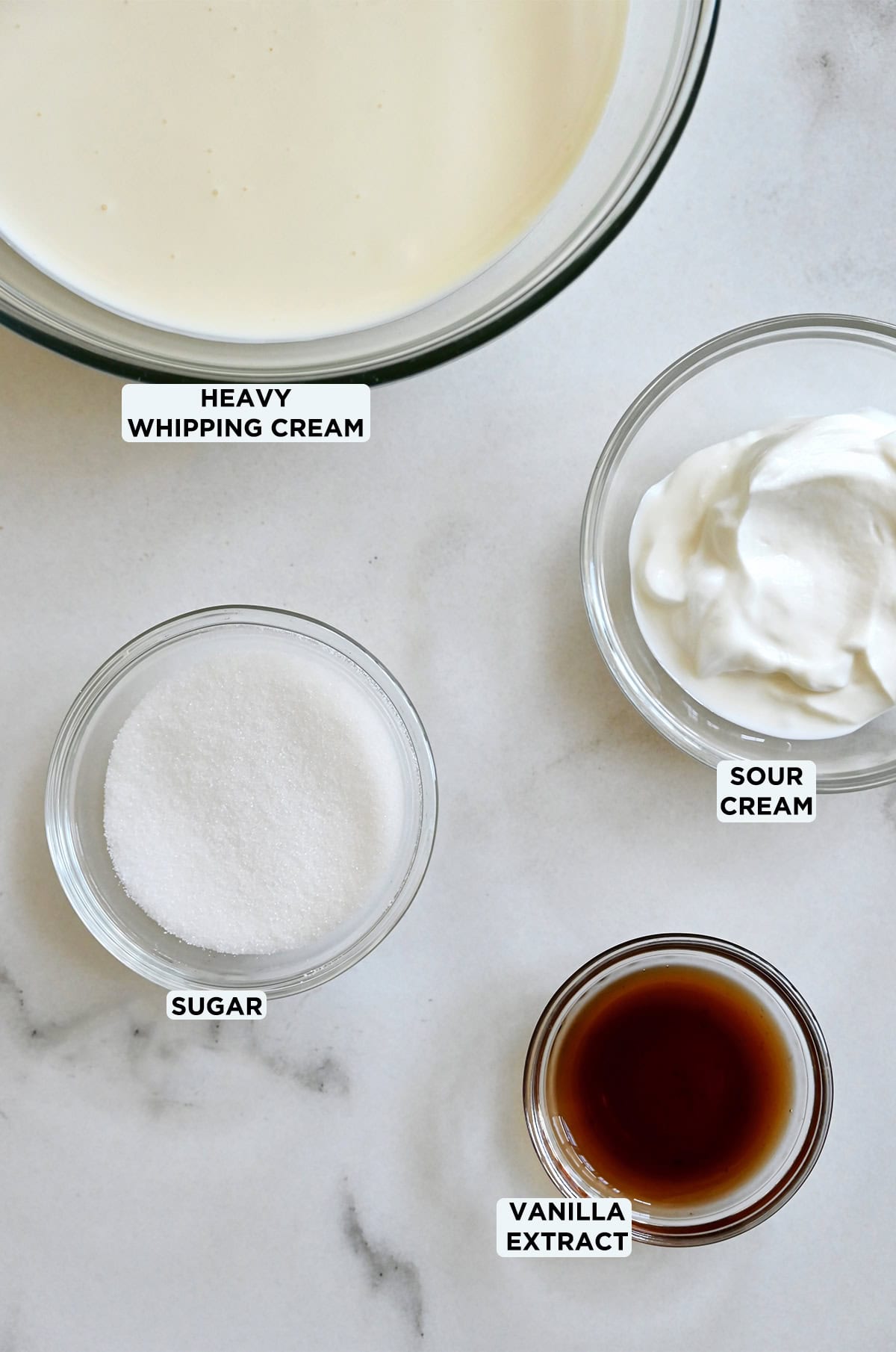 Glass bowls containing heavy cream, sour cream, sugar and vanilla extract.