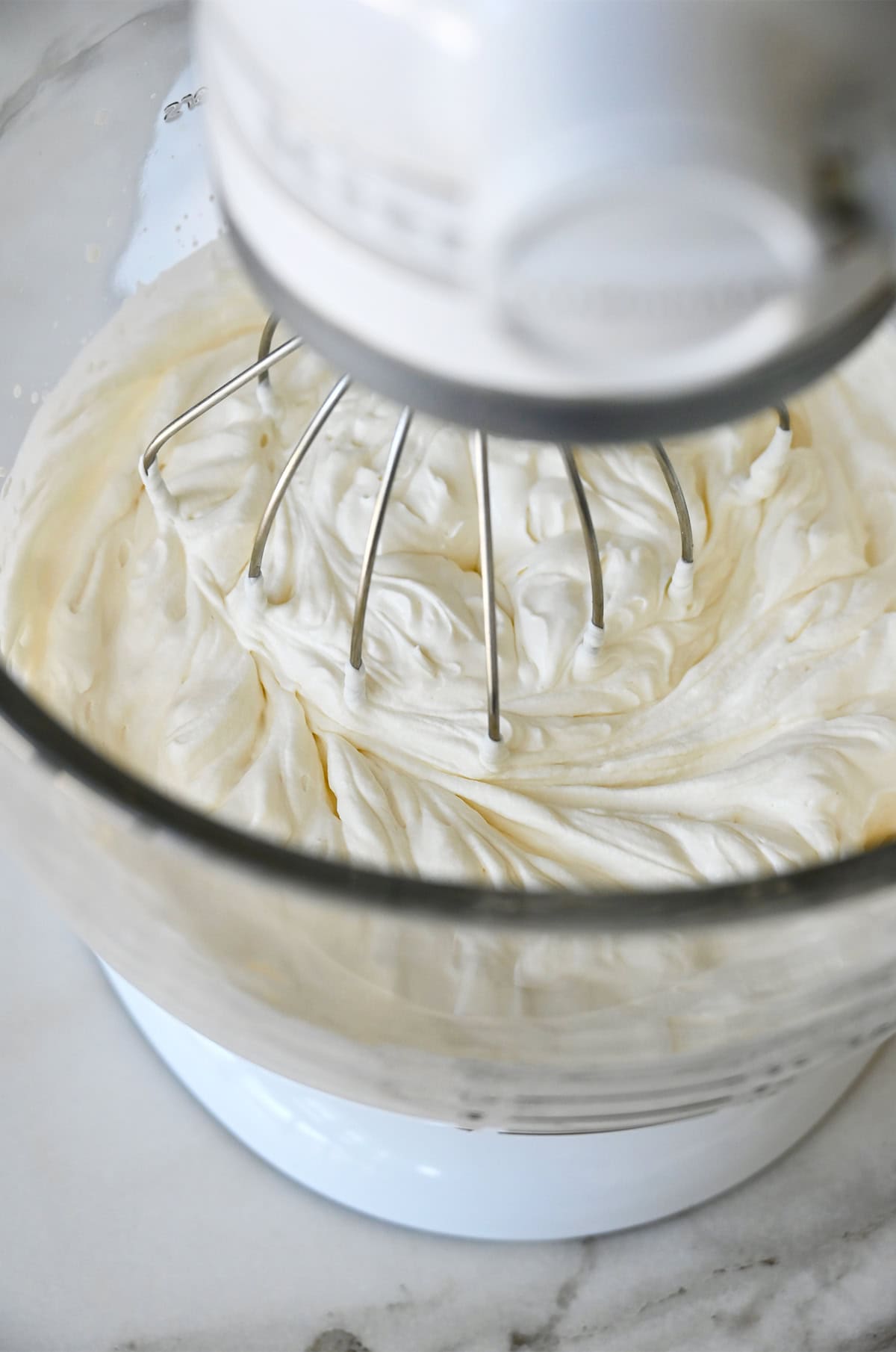Heavy whipping cream and sour cream being whipped together in a stand mixer bowl with the whisk attachment.