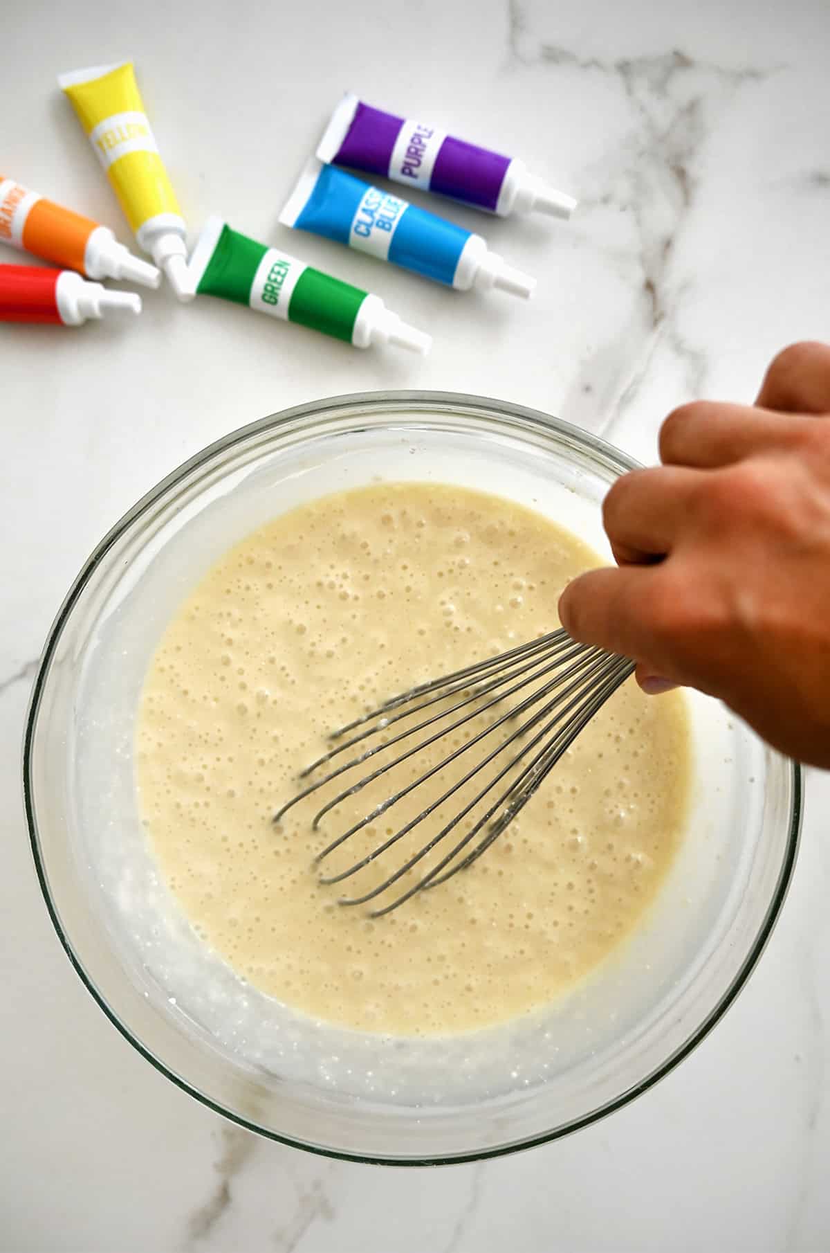 Cake mix batter in a large bowl with tubes of gel food coloring nearby.