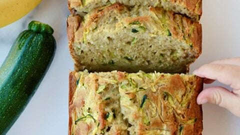 A sliced loaf of Zucchini Banana Bread with a child's hand touching it