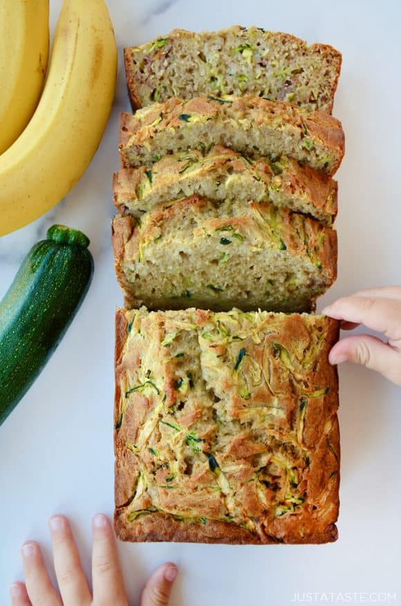 A sliced loaf of Zucchini Banana Bread with a child's hand touching it