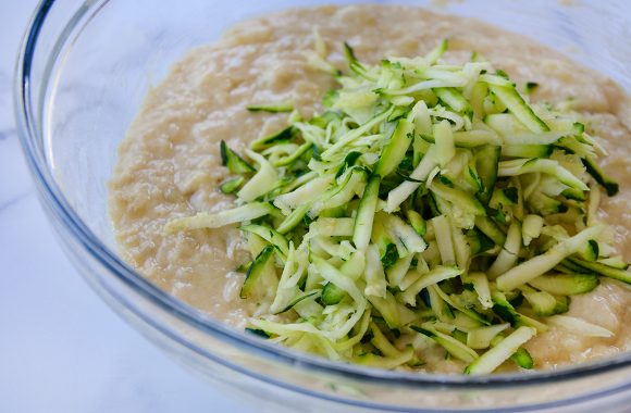 Clear bowl containing quick bread batter and shredded zucchini