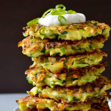 A tall stack of zucchini fritters topped with sour cream and sliced scallions.