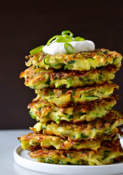 A tall stack of zucchini fritters topped with sour cream and sliced scallions.