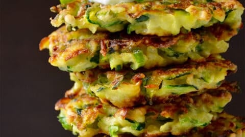A tall stack of zucchini fritters topped with sour cream and sliced scallions.
