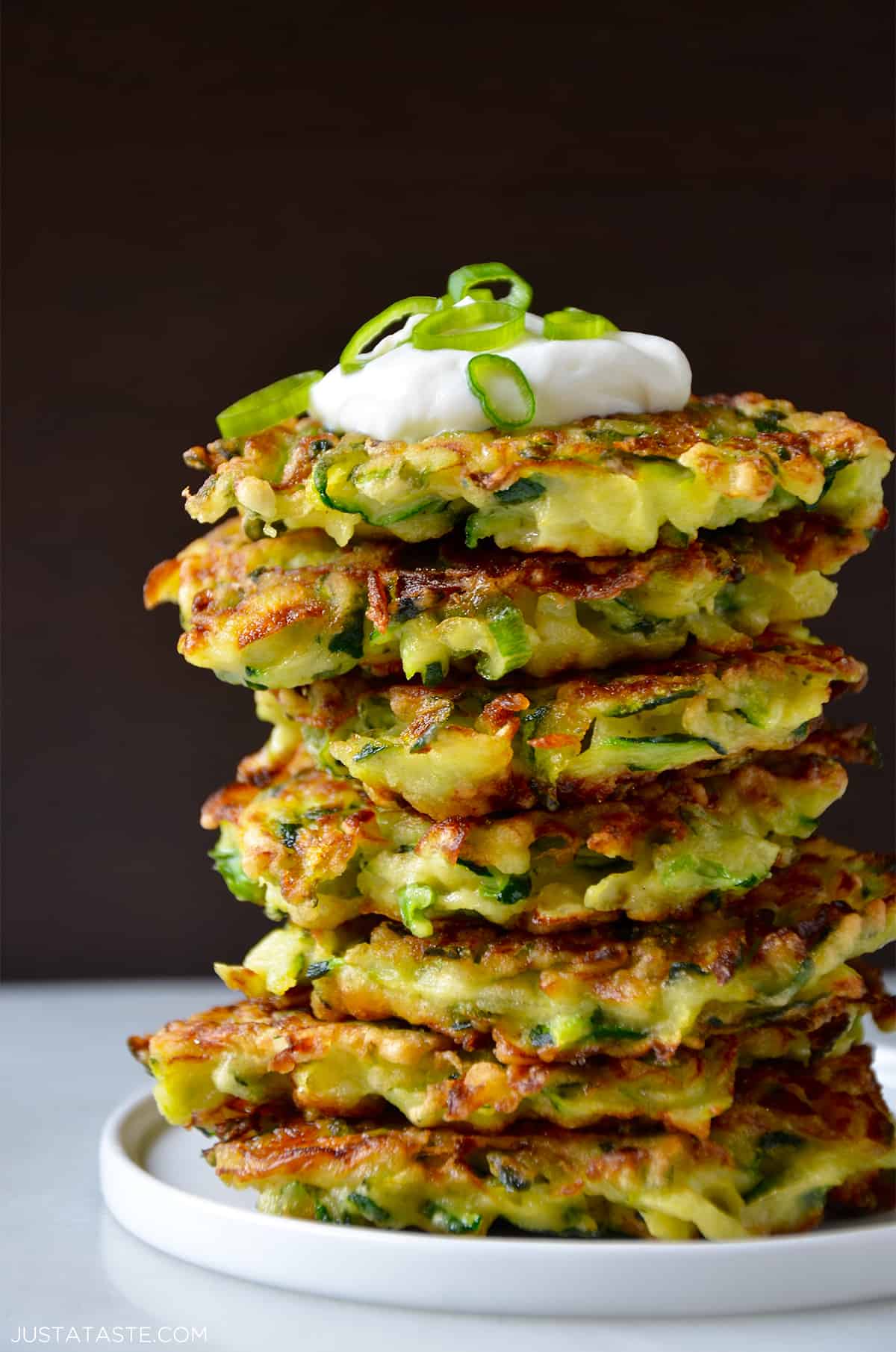 A tall stack of zucchini fritters topped with sour cream and sliced scallions.