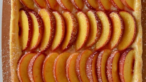 A top-down view of fresh peach slices dusted with powered sugar atop a buttery puff pastry crust.