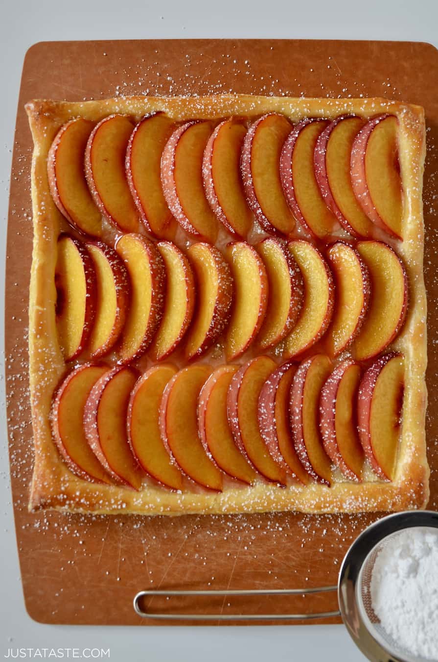 A top-down view of fresh peach slices dusted with powered sugar atop a buttery puff pastry crust.